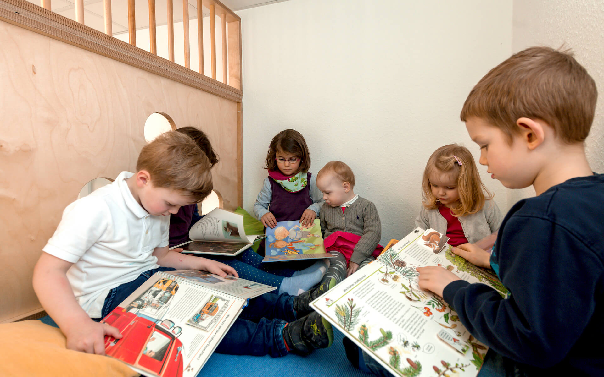 Kinder lesen gemeinsam in einer geschützten Nische unter einem eingebauten Podest aus Birkenholz