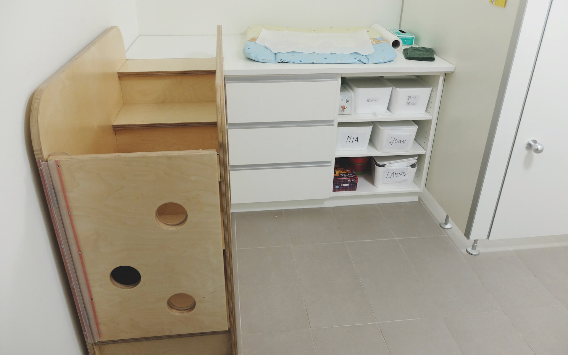 Wickeltisch mit Treppe aus Birkenholz, weißen Schubladen und offenen Fächern mit beschrifteten Boxen